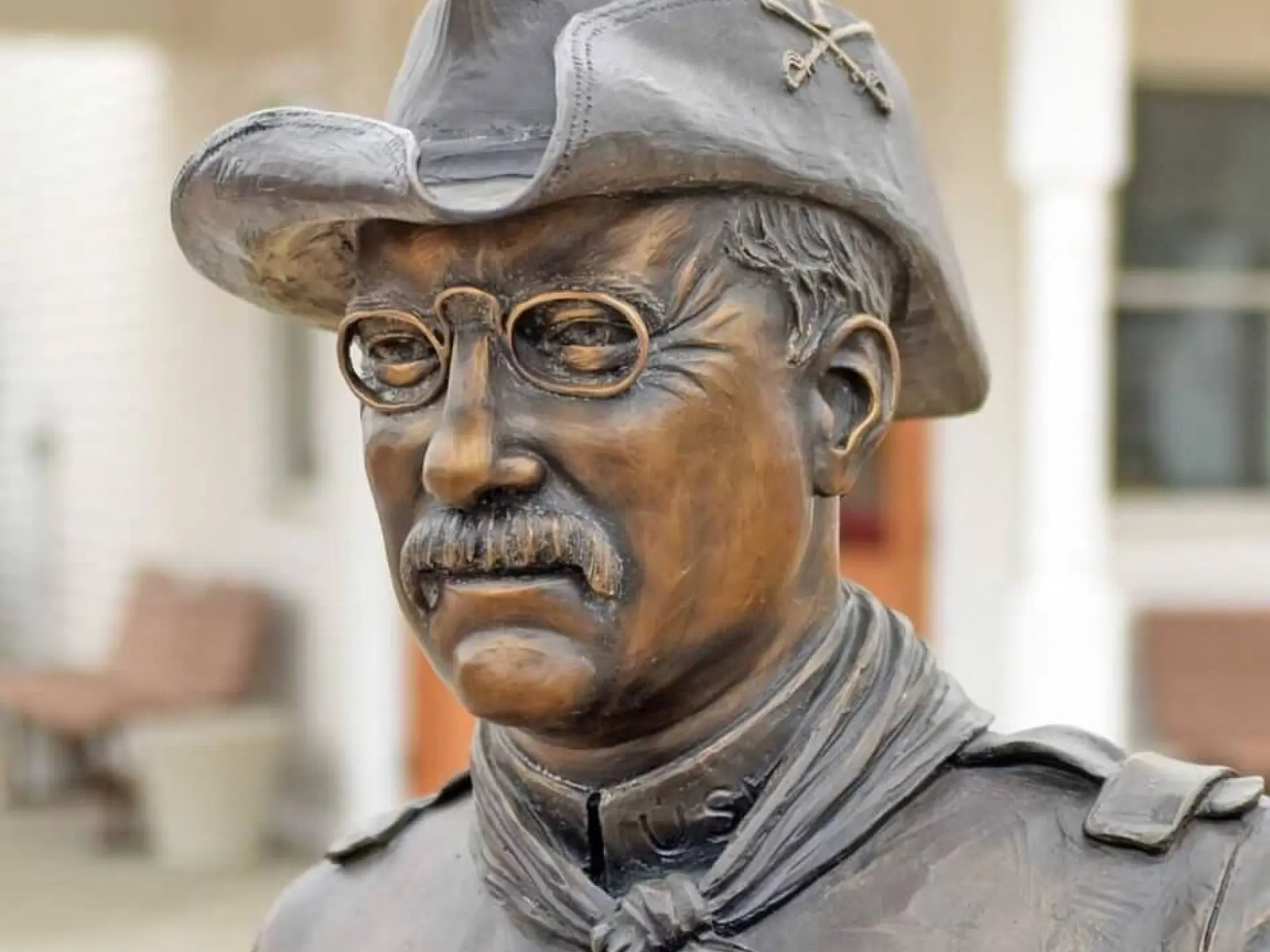 Bronze statue of a man in a hat and glasses, outdoors.